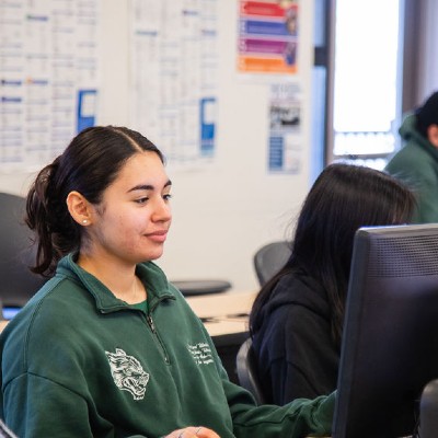 a smiling student in a classroom looking at a computer monitor