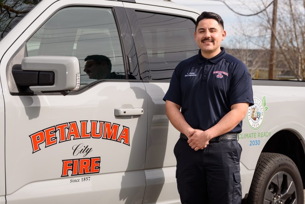 Fire Inspector L. Duran stands next to a gray pickup truck featuring the Petaluma City Fire logo on the door and a 'Climate Ready 2030' emblem on the truck bed.