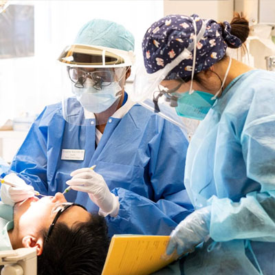 Two dental professionals in scrubs and masks working on a patient