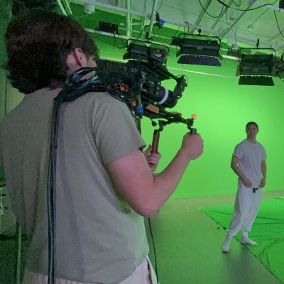a person with a movie camera pointed at a greenscreen with another person in front of it